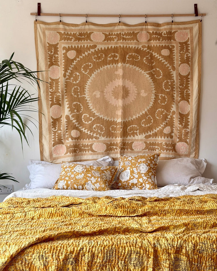 vintage suzani wall hanging in a bedfroom with yellow handmade block print bedcover and mustard floral cushions