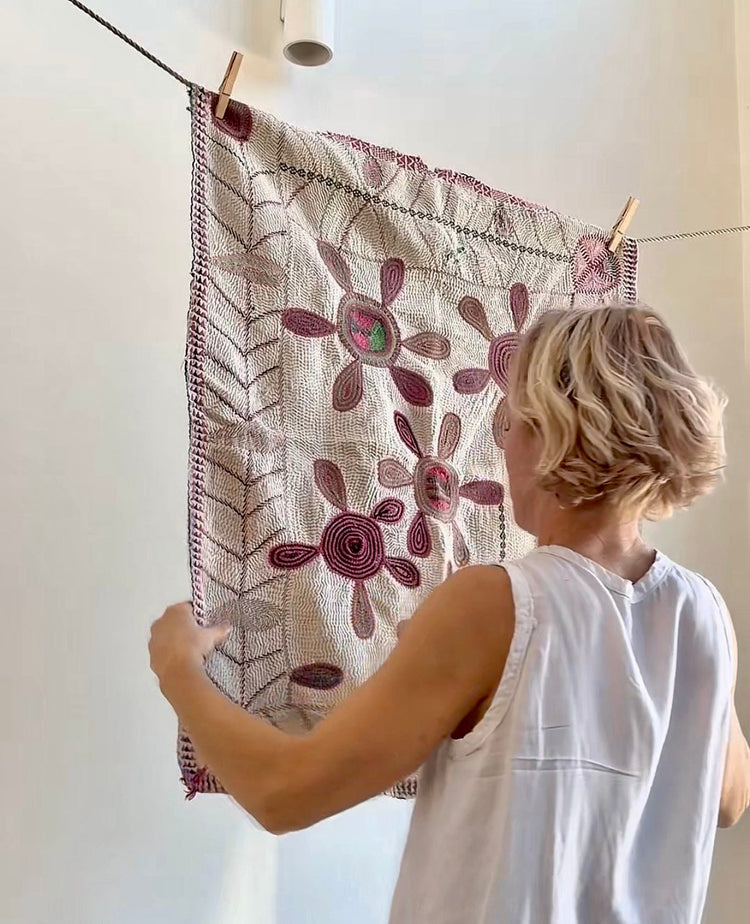 woman holding an embroidered kantha quilt in white with flowers