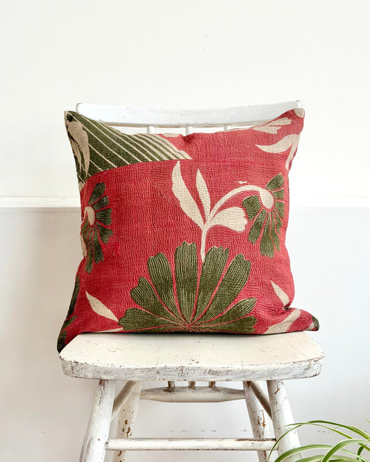 Decorative pillow with leaf pattern on a white stool against a white wall